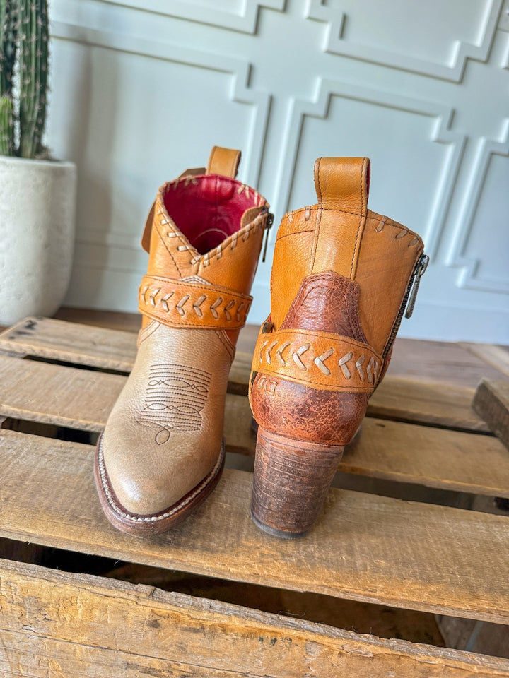 The Cadillacs by Savannah Sevens western life{&}style: tan leather western boots with decorative stitching and braided details, shown front and back on a wooden surface next to a cactus and a white paneled wall.