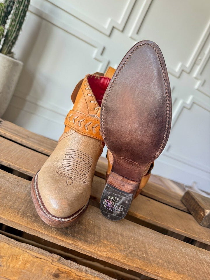 A pair of The Cadillacs western boots by Savannah Sevens western life{&}style is displayed on wood. One boot stands upright while the other shows its smooth leather sole, intricate stitching, and detailed upper pattern.