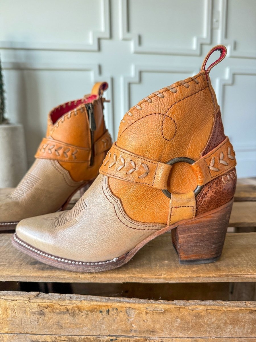 The Cadillacs by Savannah Sevens western life{&}style: tan and brown leather western boots with decorative stitching, Goodyear welt, wooden block heel, and metal ring detail. Shown on rustic wood against a white textured wall.