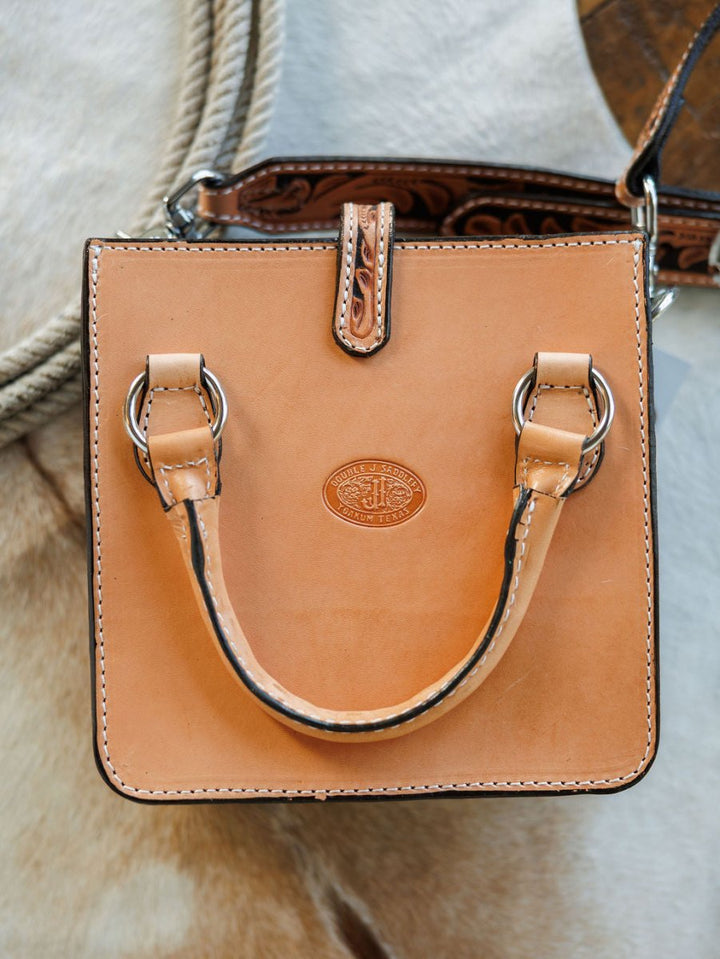 The Campitos by Savannah Sevens western life{&}style is a small, square, tan hand-tooled leather handbag with a single short handle, silver hardware, decorative stitching, and an embossed logo, shown against a light textured background. By Double J. 