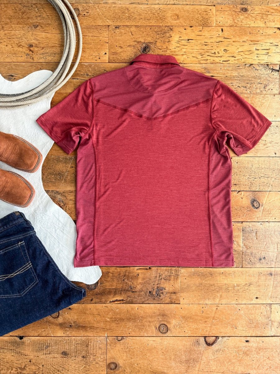 The Carlyle men's quarter button top by Savannah Sevens western life&style in red performance fabric is laid flat beside brown cowboy boots and dark blue jeans on a wooden floor.