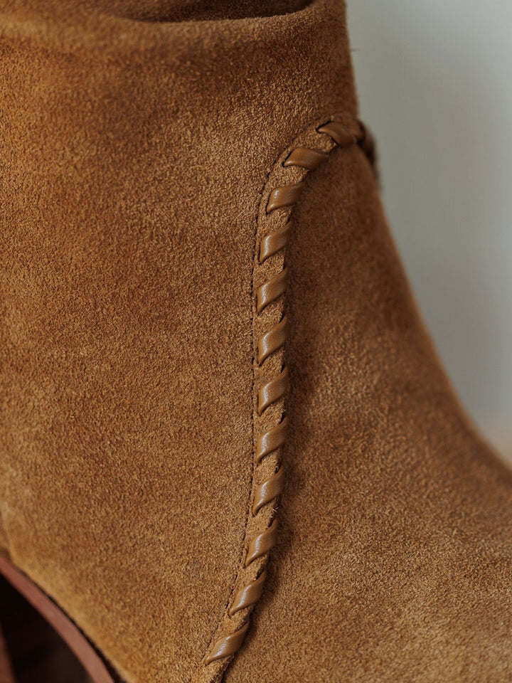 Close-up of The Cerritos by Savannah Sevens western life{&}style, a tan suede bootie with a decorative leather braid stitched along the side, showcasing its textured material, relaxed silhouette, and quality craftsmanship.