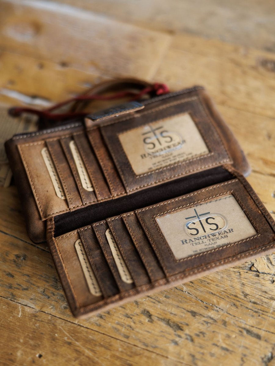The Chisholm by Savannah Sevens western life{&}style is a brown leather wristlet wallet with multiple card slots, shown open on wood and revealing two clear ID windows inside.