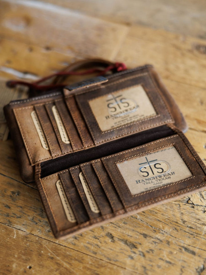 The Chisholm by Savannah Sevens western life{&}style is a brown leather wristlet wallet with multiple card slots, shown open on wood and revealing two clear ID windows inside.