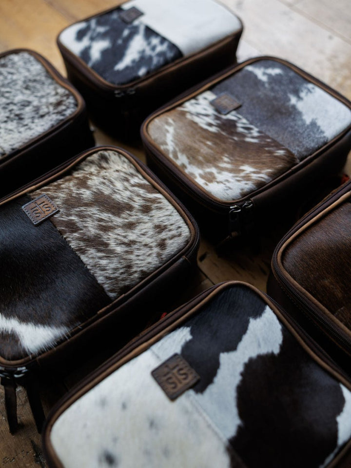 The Cowtown by Savannah Sevens western life{&}style features rectangular pouches with brown leather edges and black, white, and brown cowhide patterns—ideal as a chic makeup organizer or leather bag for stylish storage.