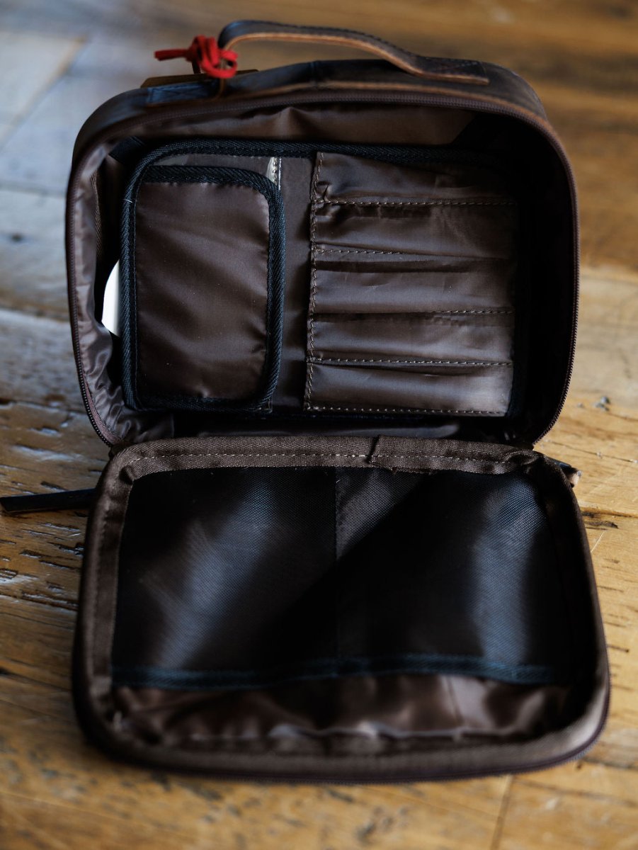 The Cowtown by Savannah Sevens western life{&}style is a brown leather makeup bag with dark lining, shown open on a wooden surface. Its multiple interior pockets and compartments offer organized storage for your essentials.
