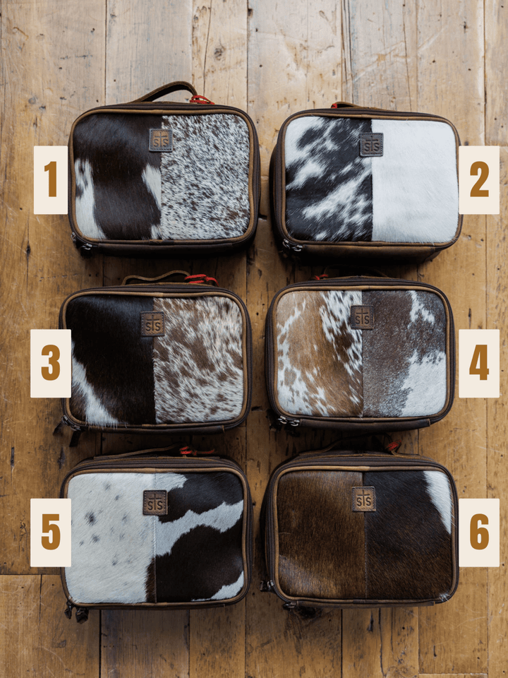 Six "The Cowtown" cowhide makeup cases by Savannah Sevens western life{&}style, each with a unique pattern, are arranged in two rows of three on a wooden floor and individually numbered 1 to 6.