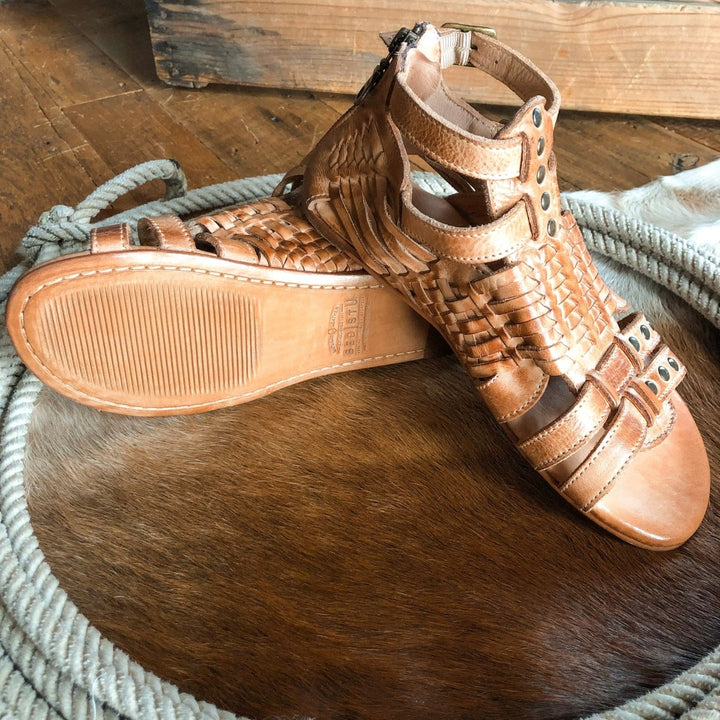 The Dacono woven leather sandals by Savannah Sevens western life{&}style, one upright and one showing the sole, are displayed on a round hide mat with a coiled rope atop a wooden floor.