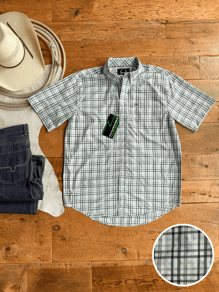 The Danville Cinch Men's Plaid Button Up by Savannah Sevens western life{&}style is laid flat on a wooden floor beside a cowboy hat and folded jeans. An inset shows its green, gray, and white moisture-wicking plaid pattern.