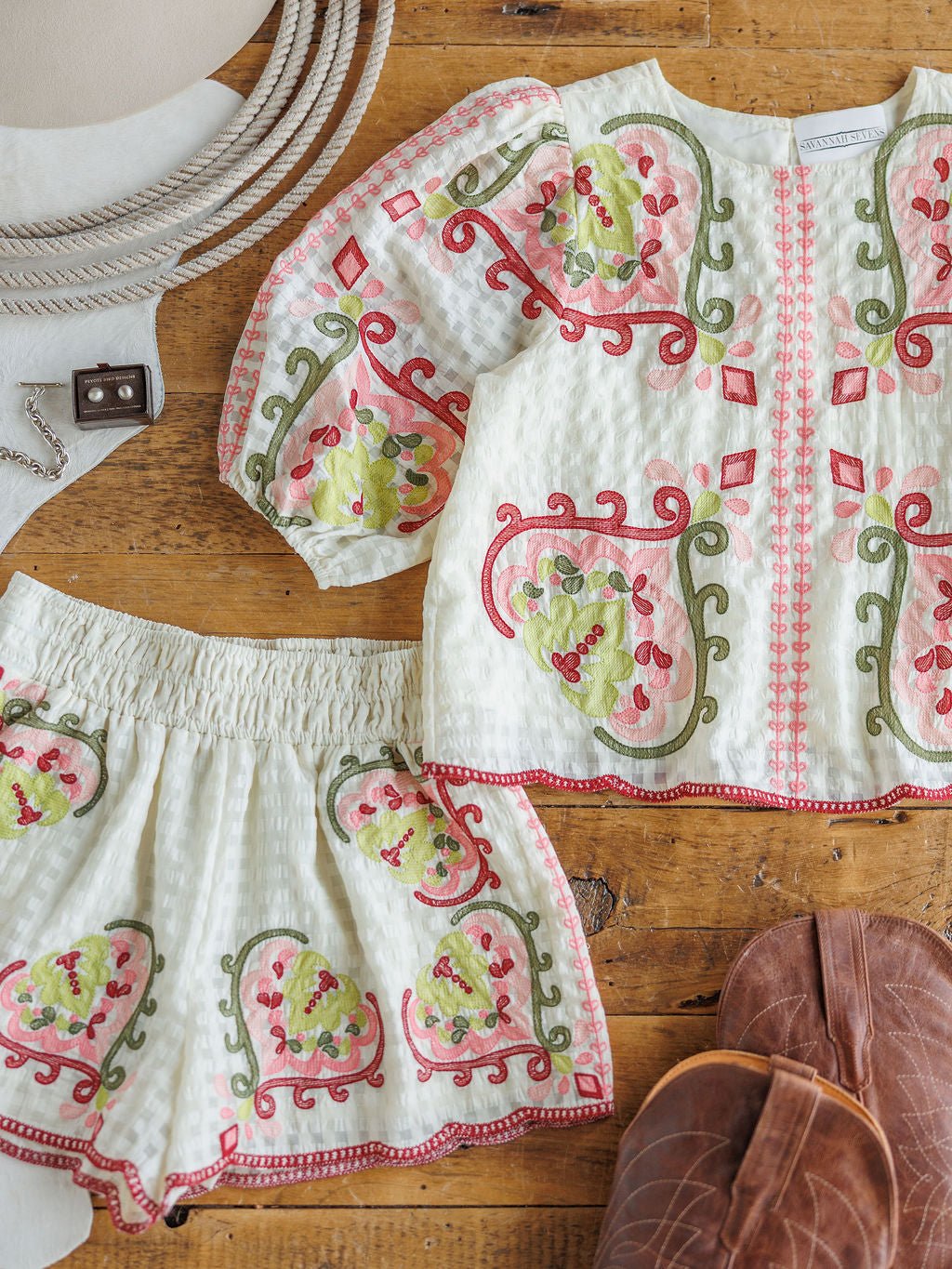 The Elrosa {Set} by Savannah Sevens western life{&}style features a white long-sleeve floral embroidered top and high-waisted shorts with vibrant red, pink, and green accents, styled on wood alongside brown sandals.