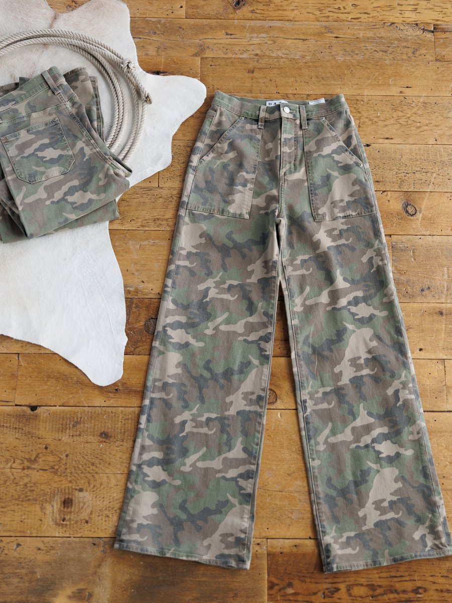 The Granger High Rise Wide Leg Jean by Savannah Sevens western life{&}style is displayed on a wooden floor, with another folded pair and a coiled rope on a white animal hide rug nearby.