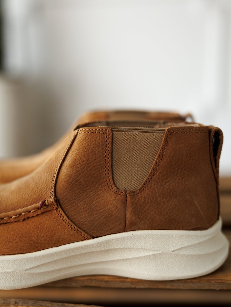 Close-up of The Holden by Savannah Sevens western life{&}style, a leather casual shoe with visible stitching, elastic side panel, and white textured slip-resistant sole, displayed on wood with a blurred neutral background.