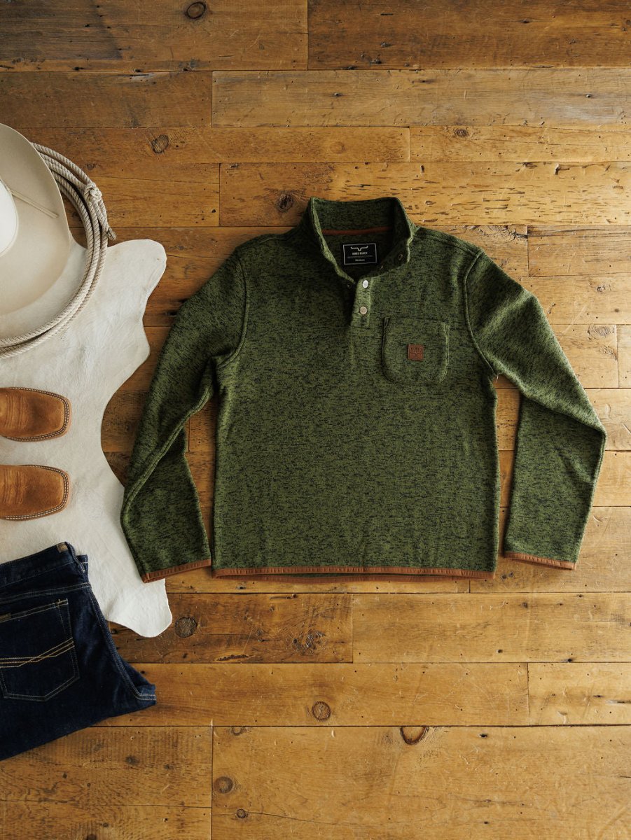 The Kempton {Men's} by Savannah Sevens western life{&}style—a green fleece-lined long-sleeve pullover with a buttoned collar—is laid on a wooden floor beside western accessories, perfect for Kimes Ranch style fans.