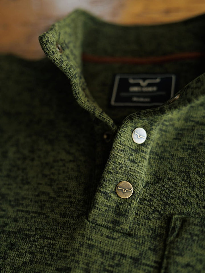 Close-up of The Kempton men's pullover by Savannah Sevens western life{&}style, showing its green textured fabric, two metal logo buttons, partially visible collar, and the shirt label inside.