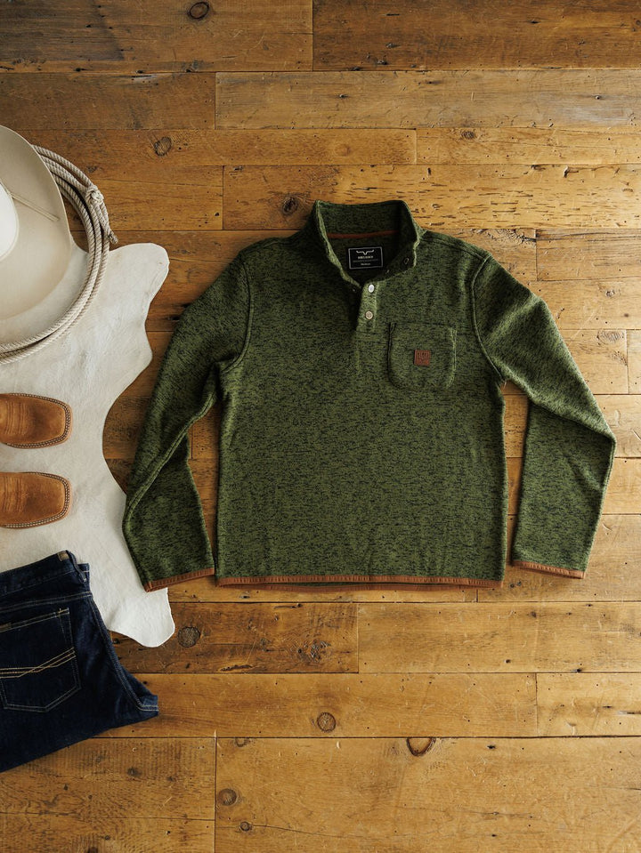 The Kempton {Men's} by Savannah Sevens western life{&}style—a green fleece-lined long-sleeve pullover with a buttoned collar—is laid on a wooden floor beside western accessories, perfect for Kimes Ranch style fans.