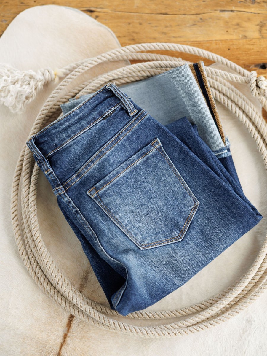 The Knox High Rise Wide Leg Jean from Savannah Sevens western life{&}style in a medium dark wash is displayed inside a coiled rope on a white fur rug, with a wooden floor in the background.