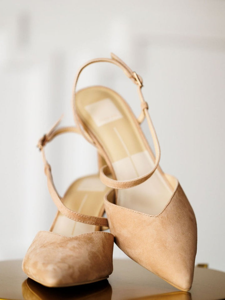 The Lafayette by Savannah Sevens western life{&}style: beige suede stiletto heels with pointed toes and adjustable buckle ankle straps, displayed with one shoe leaning against the other on a smooth surface and soft, light background.