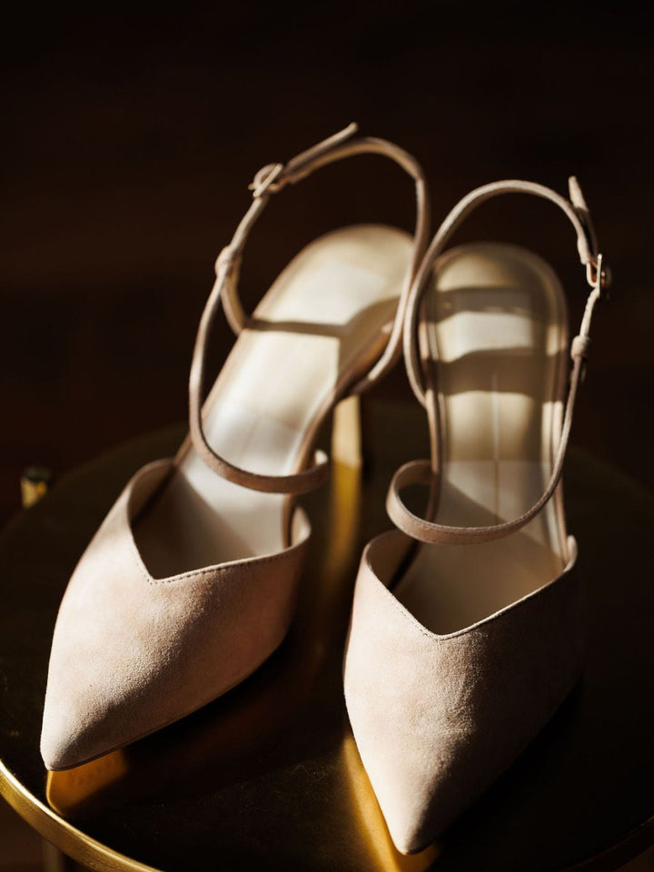 The Lafayette by Savannah Sevens western life{&}style: elegant beige suede stiletto heels with pointed toes and adjustable buckles, displayed on a golden round surface under warm lighting.