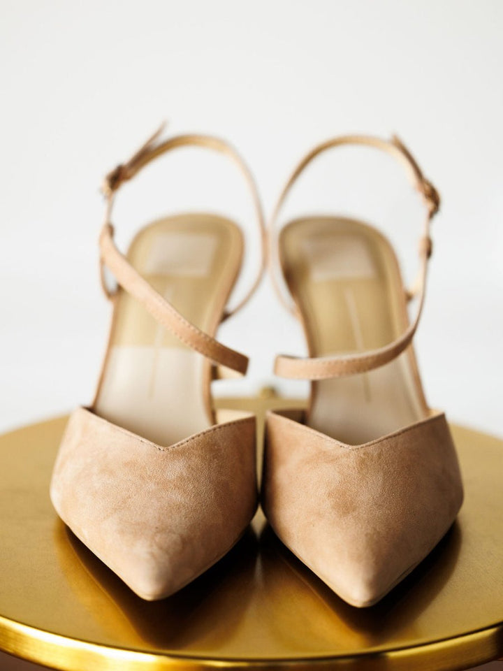 The Lafayette by Savannah Sevens western life{&}style: beige suede stiletto heels with pointed toes and adjustable buckles, shown on a round gold surface against a white background.