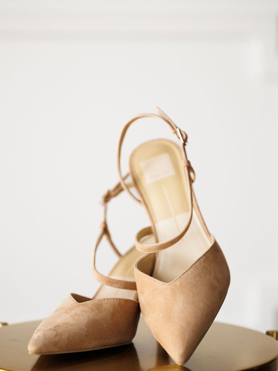 The Lafayette by Savannah Sevens western life{&}style: beige suede stiletto heels with pointed toes and adjustable buckle ankle straps, displayed on a round surface against a white background.