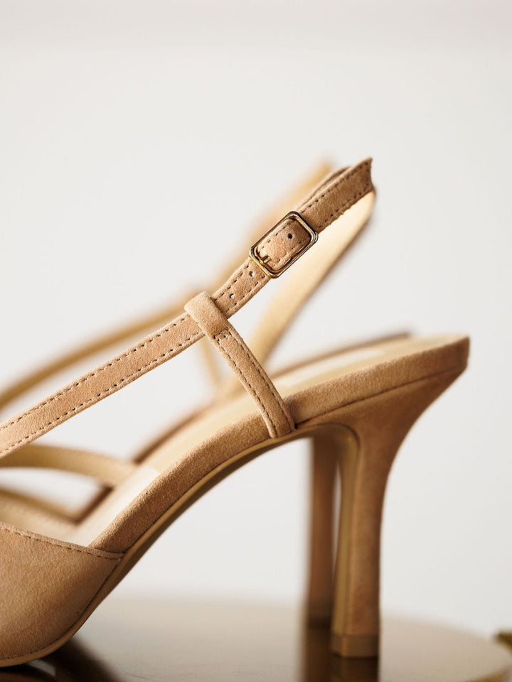 Close-up of "The Lafayette" by Savannah Sevens western life{&}style—beige suede stiletto heel sandal with an adjustable buckle slingback strap, highlighting the detailed strap and heel against a neutral background.