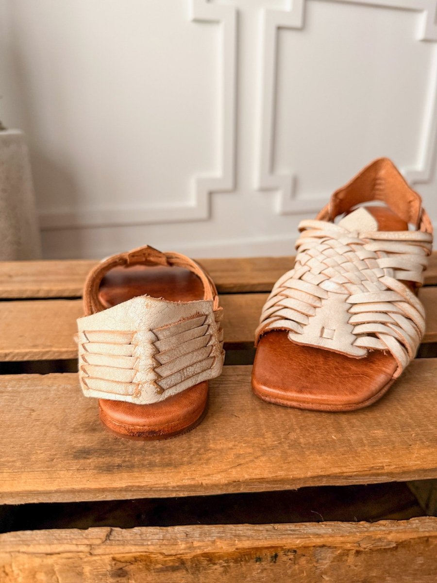 The Layton by Savannah Sevens western life{&}style: a pair of handwoven leather huarache sandals, one facing forward and one backward, displayed on wood with a white wall backdrop. Sandals made by BedStu.
