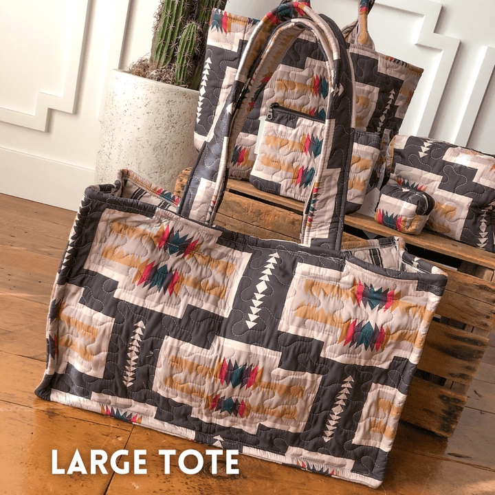 The Muskogee {Collection} by Savannah Sevens western life{&}style: a large southwest quilted tote with geometric and feather-like patterns in gray, beige, red, and turquoise. Sturdy handles for daily use. "LARGE TOTE" text appears at the bottom left.