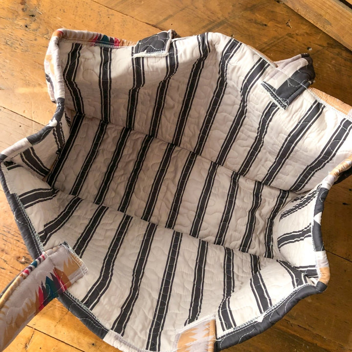 The Muskogee {Collection} by Savannah Sevens western life{&}style features a southwest quilted bag with black and white stripes inside, open on wood. Vibrant multicolored handles and edges blend classic style with true western bag charm.