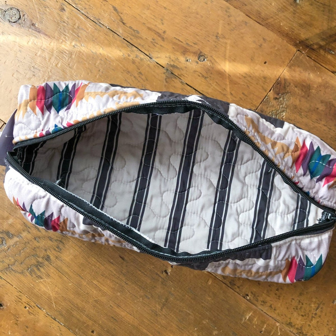 The Muskogee bag from Savannah Sevens western life{&}style features a colorful triangular pattern, a striped lining, and a zippered opening. Shown open on wood, it brings Southwest quilted style from The Muskogee {Collection}. By Ida Mae. 