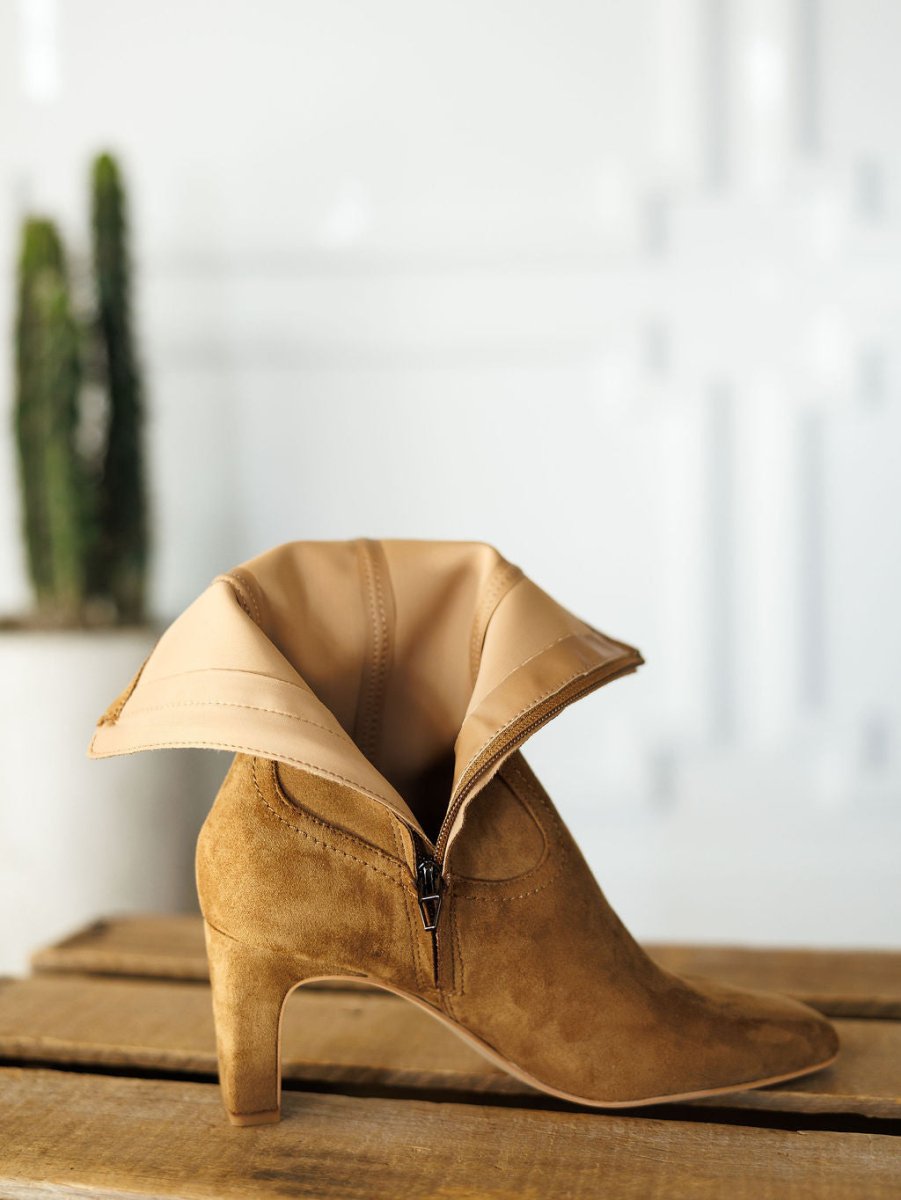The Palmetto bootie by Savannah Sevens western life{&}style, in tan faux suede with a side zipper, is displayed unzipped and folded open on a wooden surface with a blurred cactus in the background.