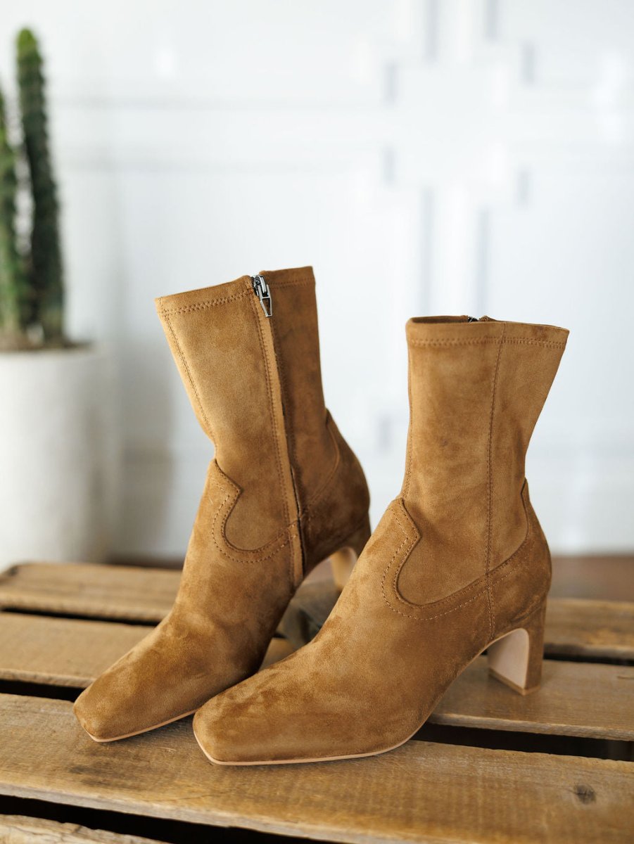 The Palmetto booties by Savannah Sevens western life{&}style feature tan faux suede, heeled square toes, and side zippers. Shown on a wooden surface with a blurred cactus and white wall in the background.