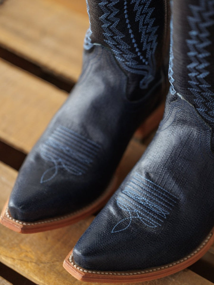 Close-up of The Pasadena boots by Savannah Sevens western life{&}style in midnight navy leather with blue stitching and a western snip toe, displayed on a wooden surface.