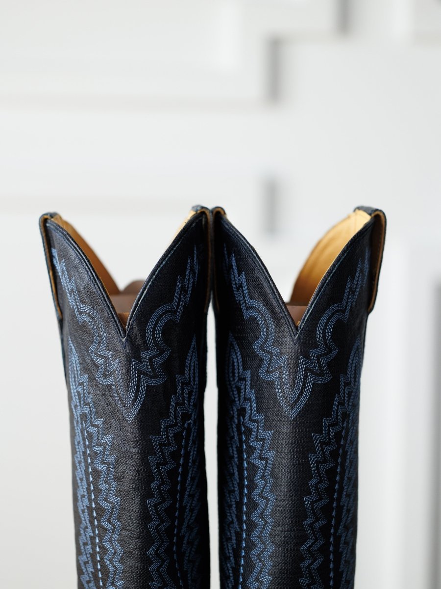 Close-up of the tops of The Pasadena boots by Savannah Sevens western life{&}style, crafted from midnight navy leather with detailed blue stitching, shown against a blurred white background.