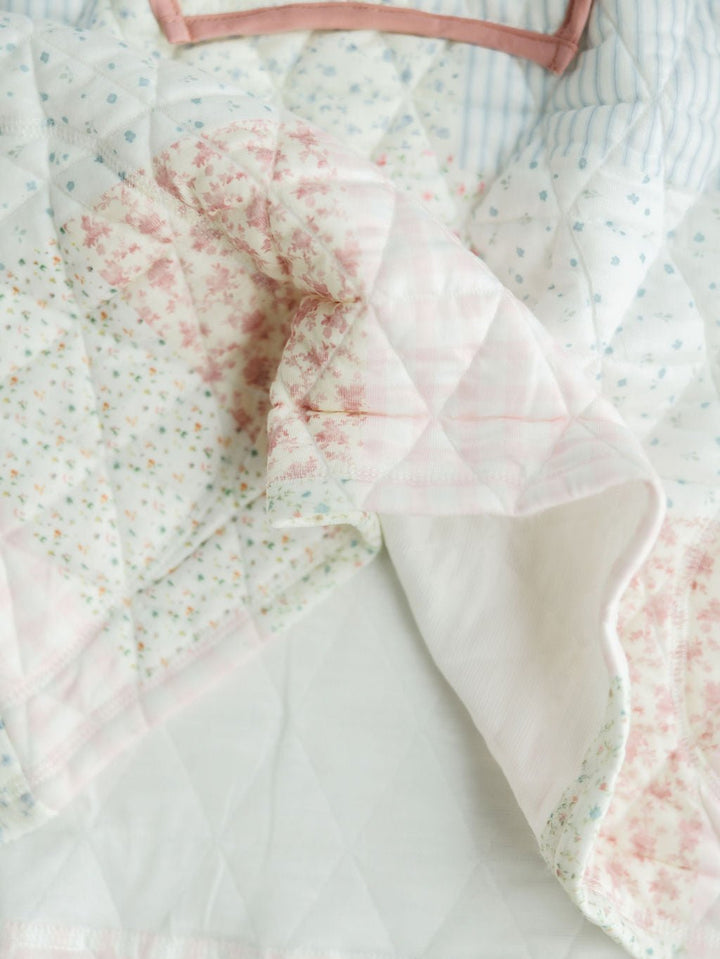 A close-up of The Petaluma {Set} by Savannah Sevens western life{&}style features quilted patchwork with pastel floral and striped patterns in pink, blue, and white, highlighting its soft folds and delicate stitching.