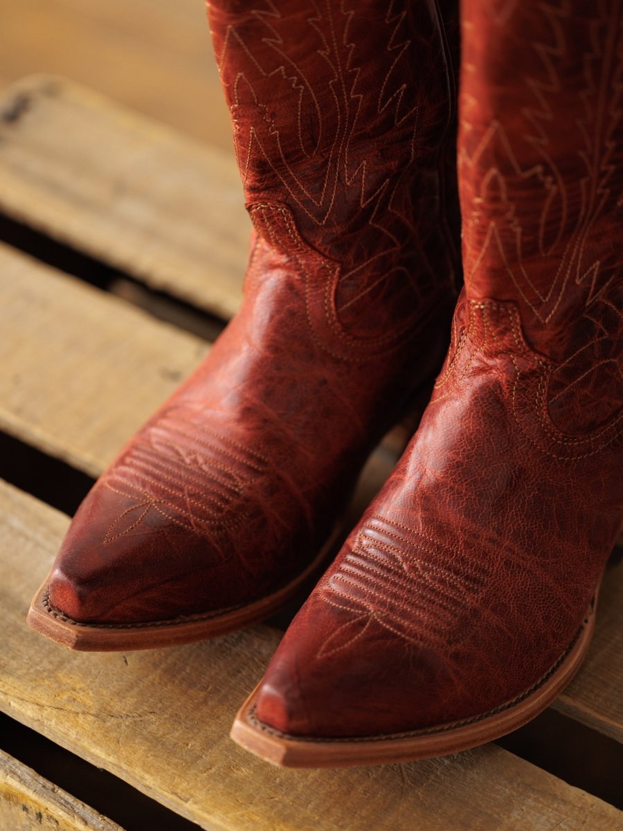 A close-up of The Pueblo distressed leather western boots by Savannah Sevens western life{&}style, featuring decorative stitching, displayed on a wooden pallet.