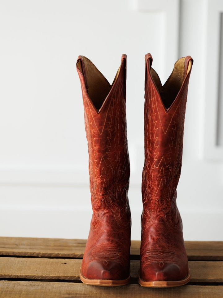 The Pueblo boots from Savannah Sevens western life{&}style are tall, distressed leather western boots with decorative stitching, standing upright on a wooden surface against a white background. Boots made by Black Star. 