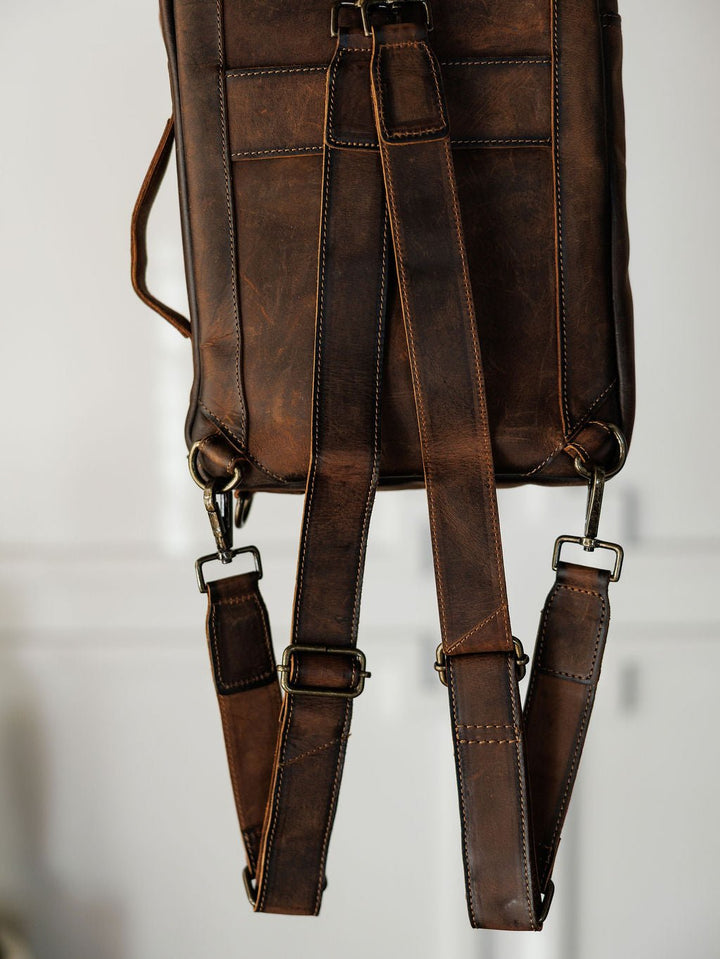 A close-up of The Ranch Hand by Savannah Sevens western life{&}style highlights its genuine leather, adjustable shoulder straps, and metal buckles against a softly blurred background.