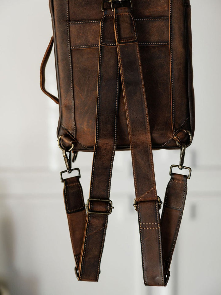 A close-up of The Ranch Hand by Savannah Sevens western life{&}style highlights its genuine leather, adjustable shoulder straps, and metal buckles against a softly blurred background.