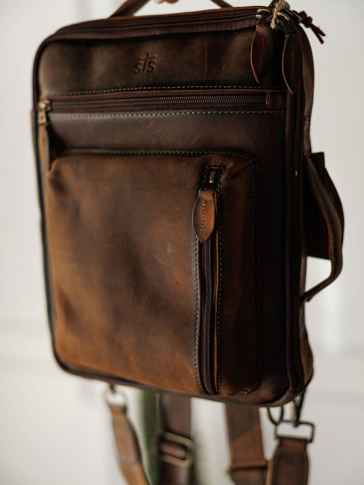 The Ranch Hand by Savannah Sevens western life{&}style: a brown genuine leather messenger bag with multiple zippered pockets, detailed stitching, and adjustable straps. Perfect laptop bag for daily use, shown hanging against a light background.