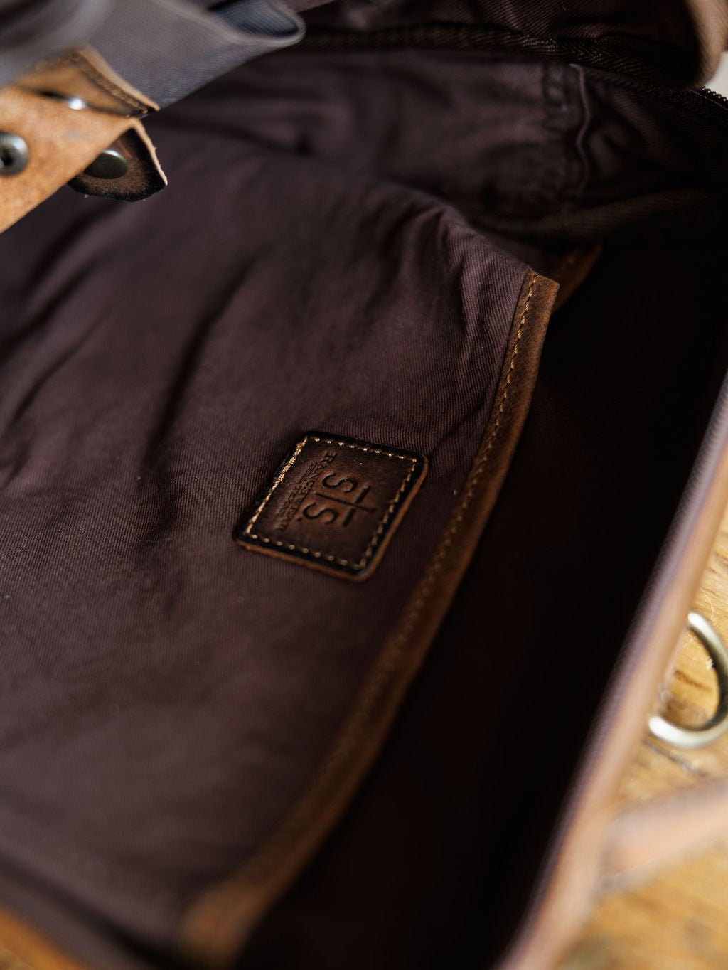 Close-up of The Ranch Hand by Savannah Sevens western life{&}style, showing the genuine leather interior with a stitched patch embossed with 315, lining details, and part of a metal clasp. By STS> 