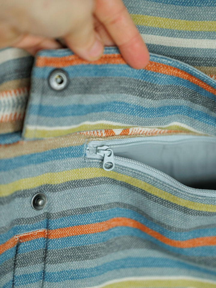 A hand opens a snap-button pocket on The Sallisaw by Savannah Sevens western life{&}style, revealing an inner zippered pocket. The striped fabric features southwest quarter snap styling in blue, orange, yellow, and gray tones.