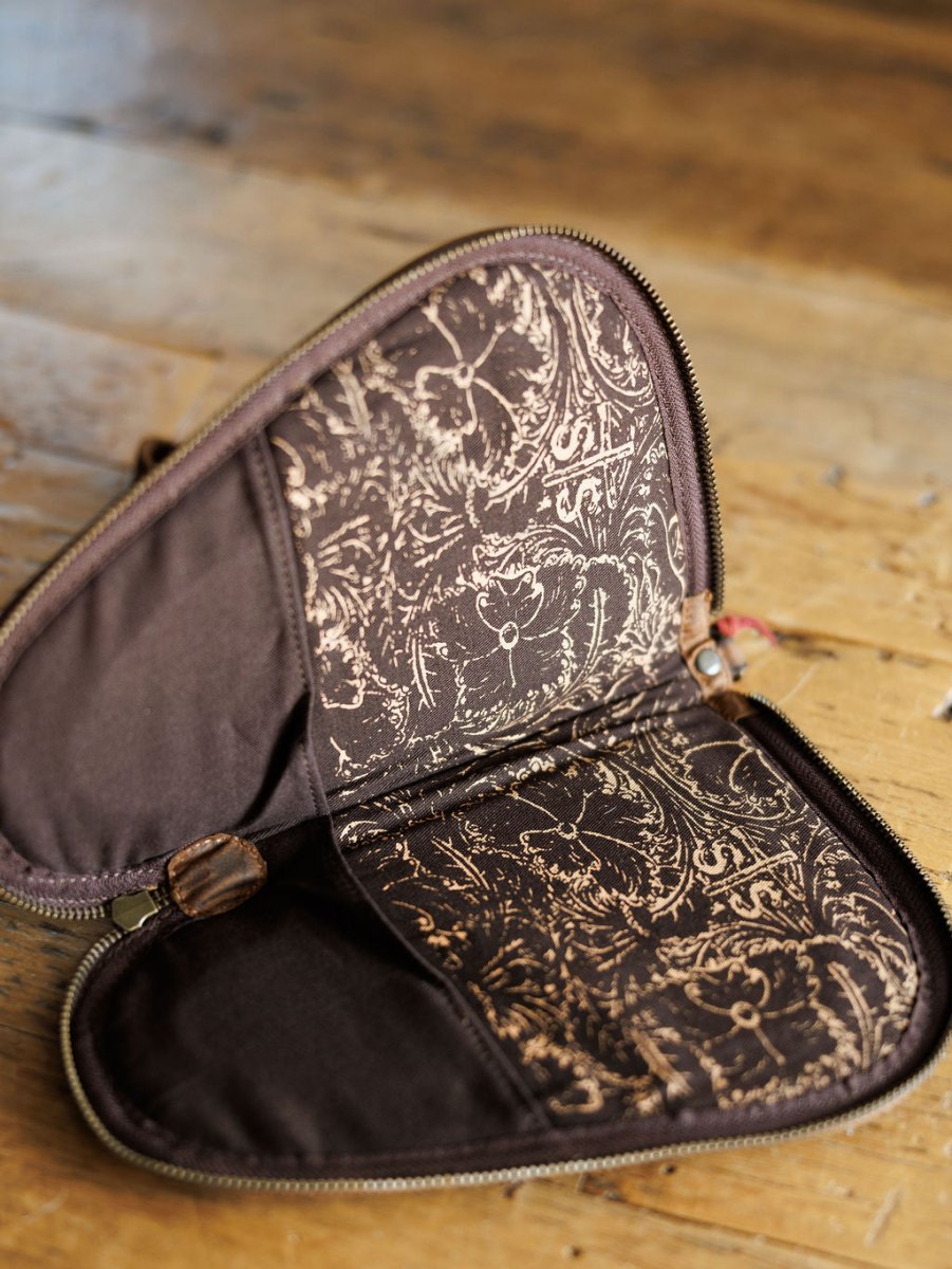 The San Antonio by Savannah Sevens western life{&}style is an open brown leather pistol case with intricate light-colored patterned lining and two inner compartments, shown on a wooden surface.