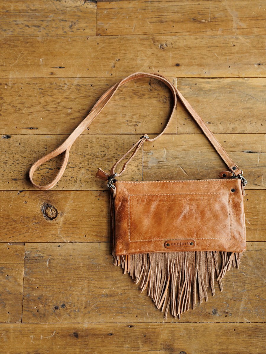 The Tahama by Savannah Sevens western life{&}style is a tan leather fringe crossbody with a long strap, shown on a rustic wooden surface.