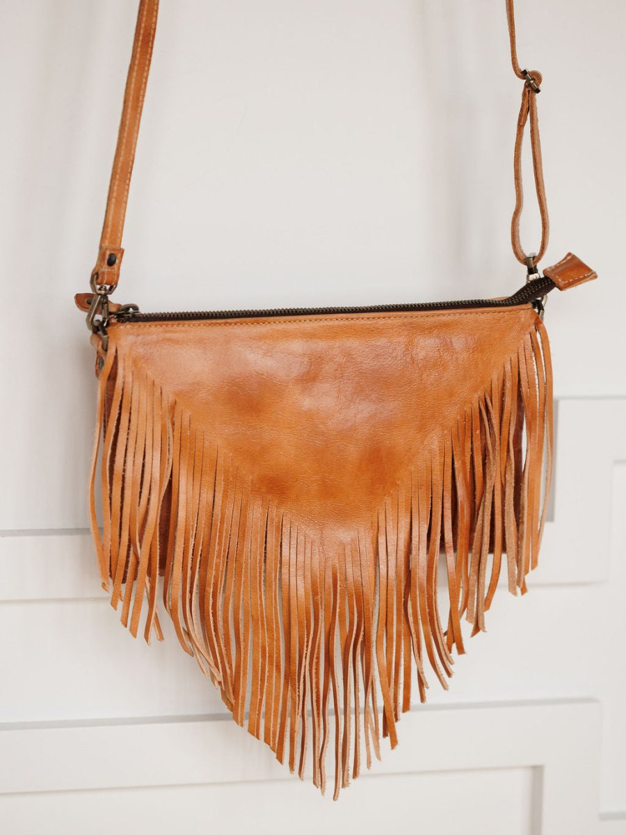 The Tahama by Savannah Sevens western life{&}style is a triangular fringe leather crossbody bag, with long fringe detail hanging from the bottom, shown against a white background.