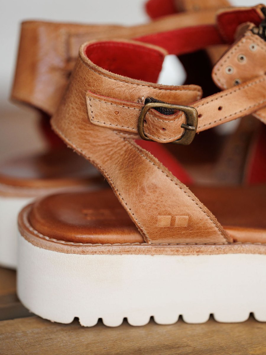 Close-up of The Tayten by Savannah Sevens western life{&}style: a distressed leather sandal with brass buckle, thick white platform sole, and red inner lining, showcasing detailed texture and stitching. Sandals made by BedStu.