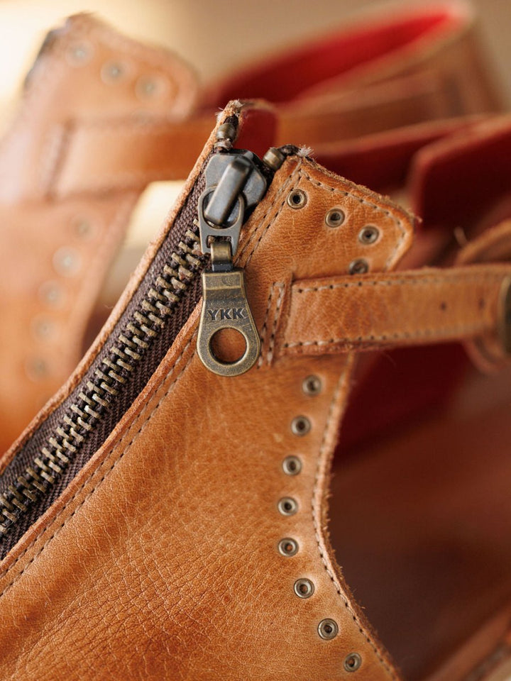 Close-up of The Tayten sandal by Savannah Sevens western life{&}style, featuring brown distressed leather, a partially unzipped metal YKK zipper, detailed stitching, and rivets along the edge. Sandals made by BedStu.