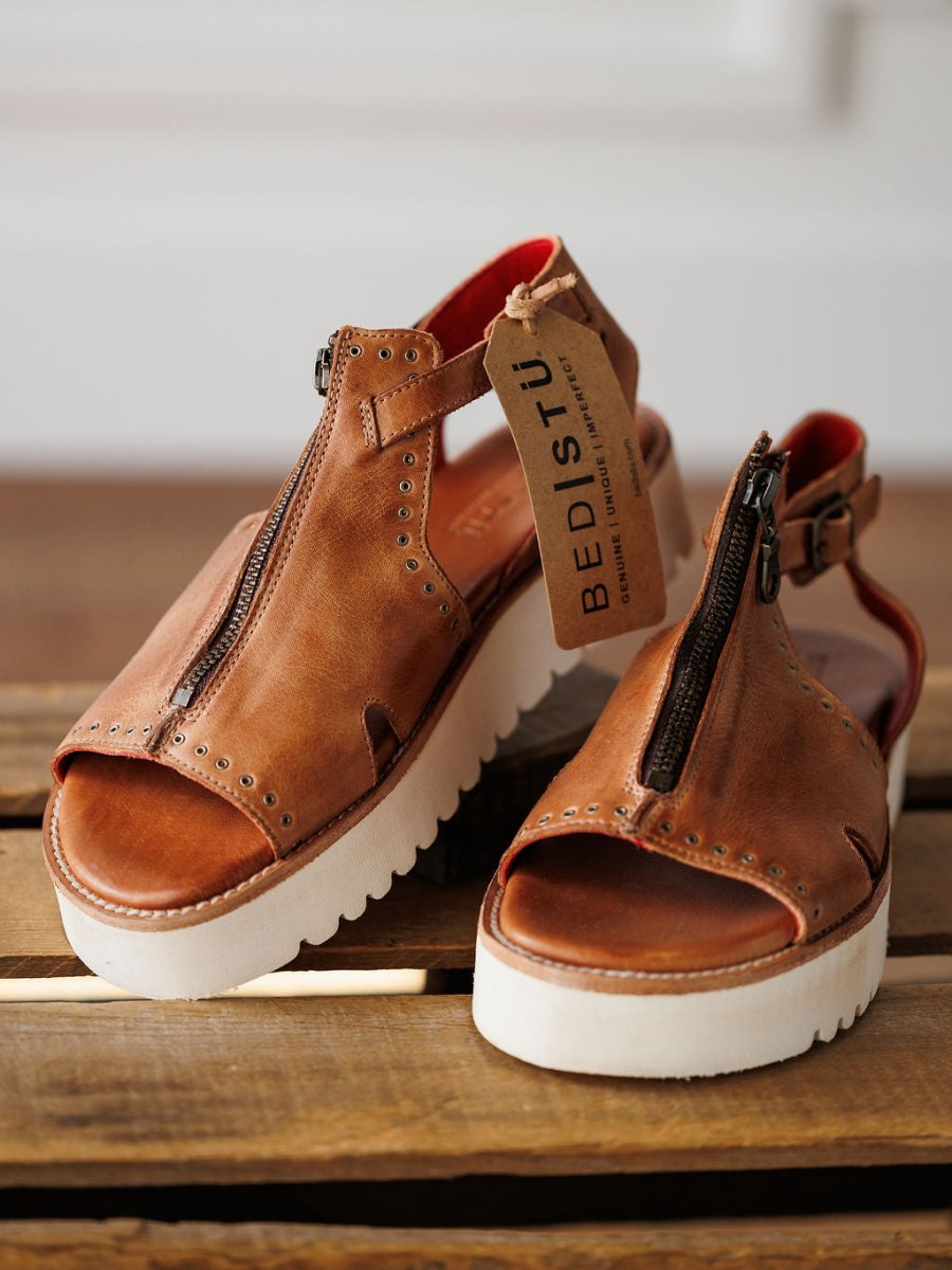 The Tayten by Savannah Sevens western life{&}style: brown distressed leather platform sandals with bold front zippers and metal rivets, shown on wood with the brand tag attached.