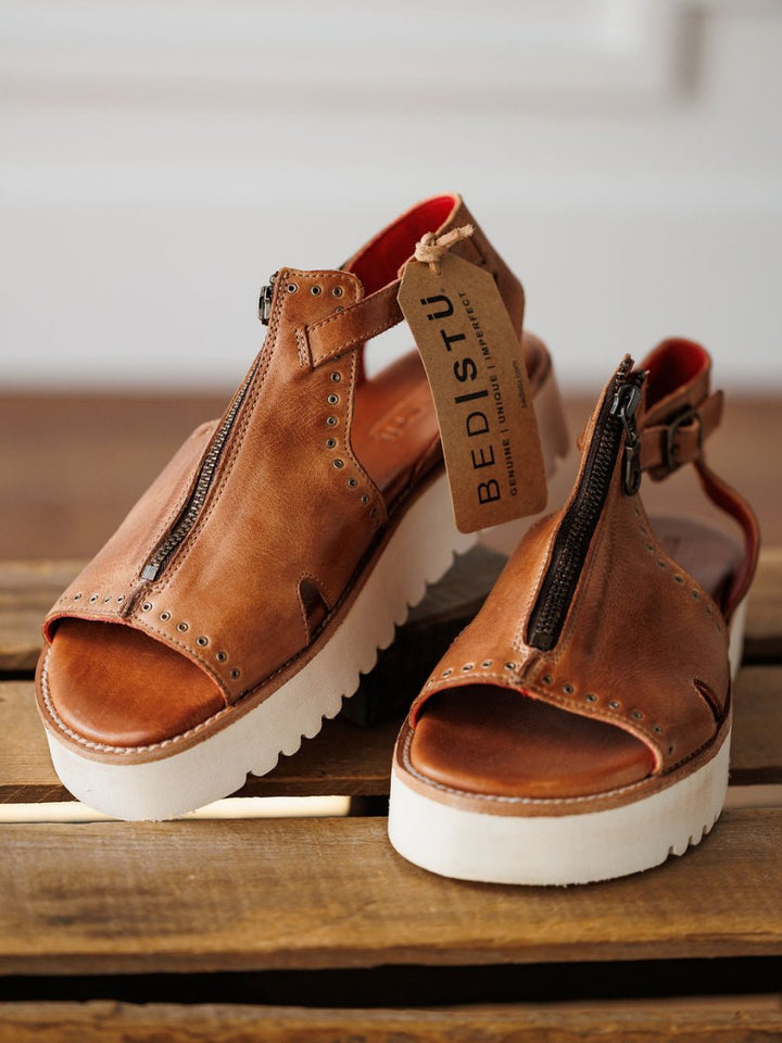 The Tayten by Savannah Sevens western life{&}style: brown distressed leather platform sandals with bold front zippers and metal rivets, shown on wood with the brand tag attached.