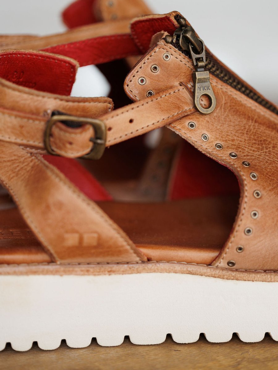 Close-up of The Tayten by Savannah Sevens western life{&}style: tan leather sandal with metal buckle, zipper, and rivet accents, red lining, and a thick white ridged platform sole. Sandals made by BedStu.