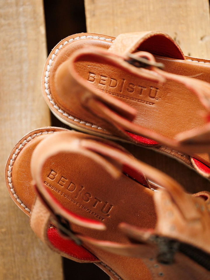 Close-up view of two distressed leather sandals with visible stitching and The Tayten by Savannah Sevens western life{&}style embossed on the insoles, placed on a wooden surface. Sandals made by BedStu.